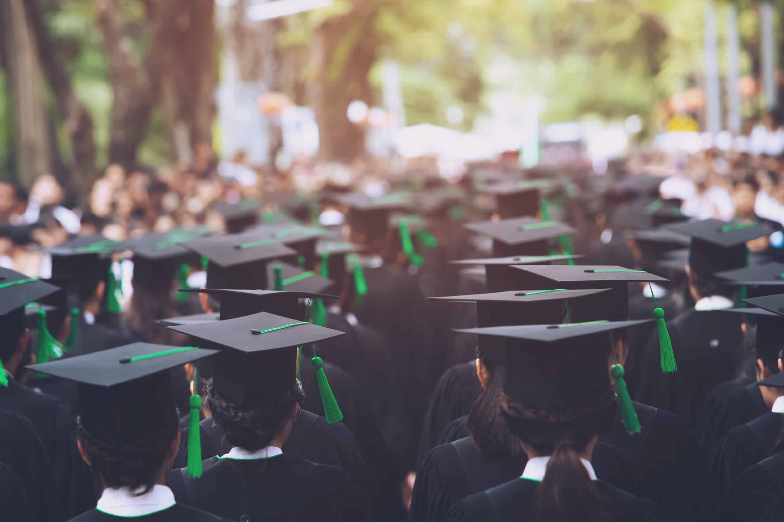 Graduates in caps and gowns during a college graduation ceremony, celebrating higher education achievement in an outdoor setting.
