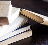 Students studying with textbooks and notebooks stacked on a table at a college campus.