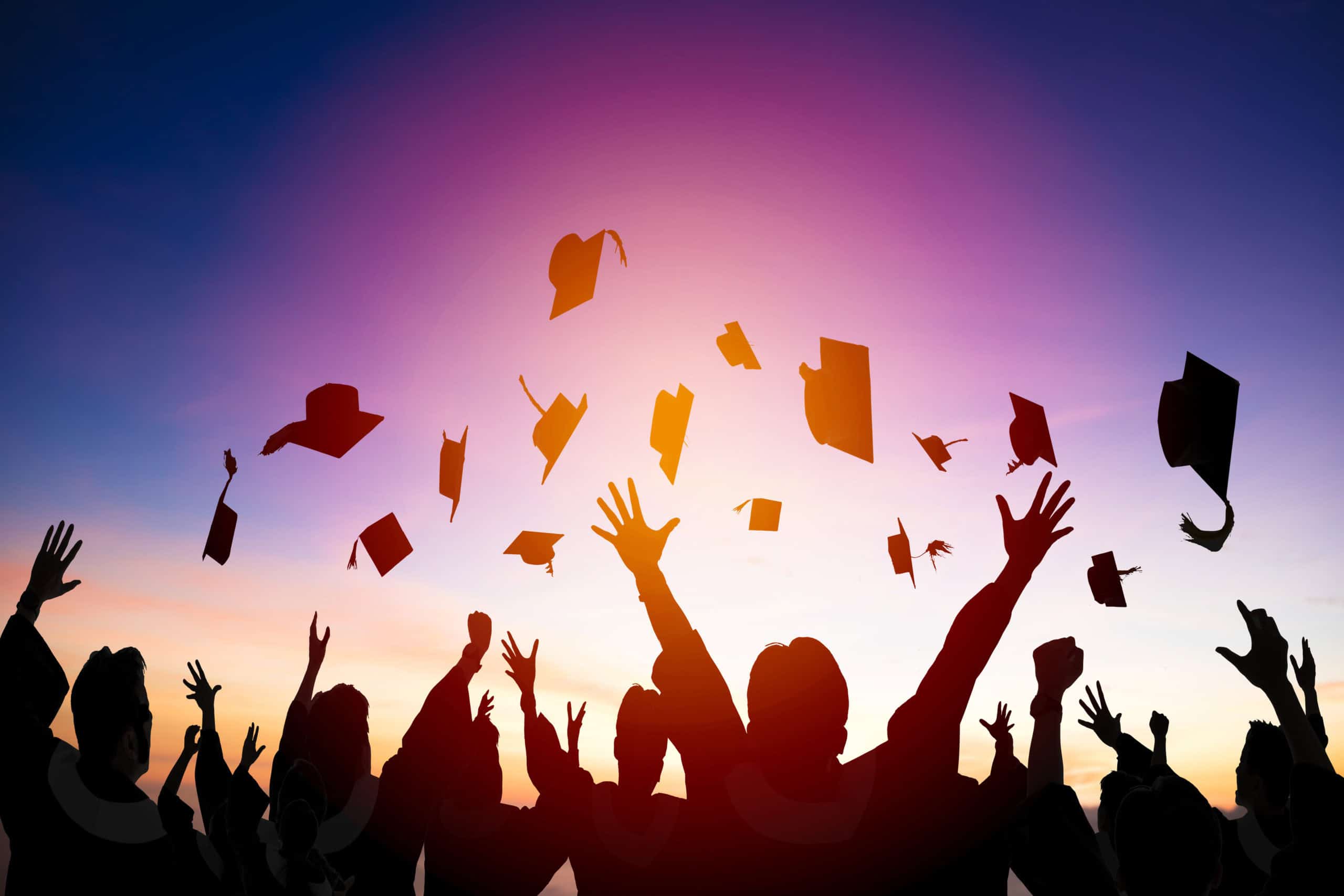 Graduates celebrating during sunset, tossing caps in the air, representing higher education success and graduation achievement.