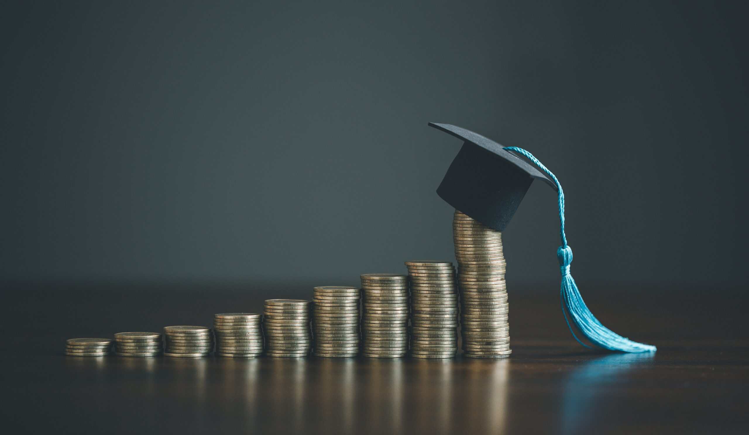 Stacked coins forming an upward trend with a graduation cap on top symbolize education funding, college success, and financial growth in higher education.