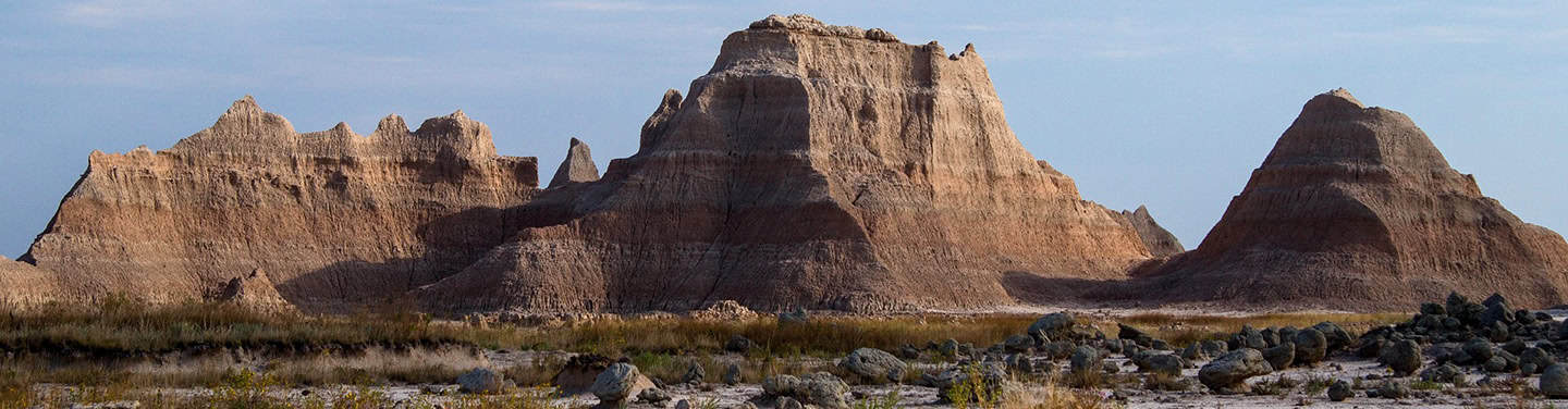 Rust-colored layered mountains of the Badlands under a clear sky, representing natural beauty and geological history in South Dakota.