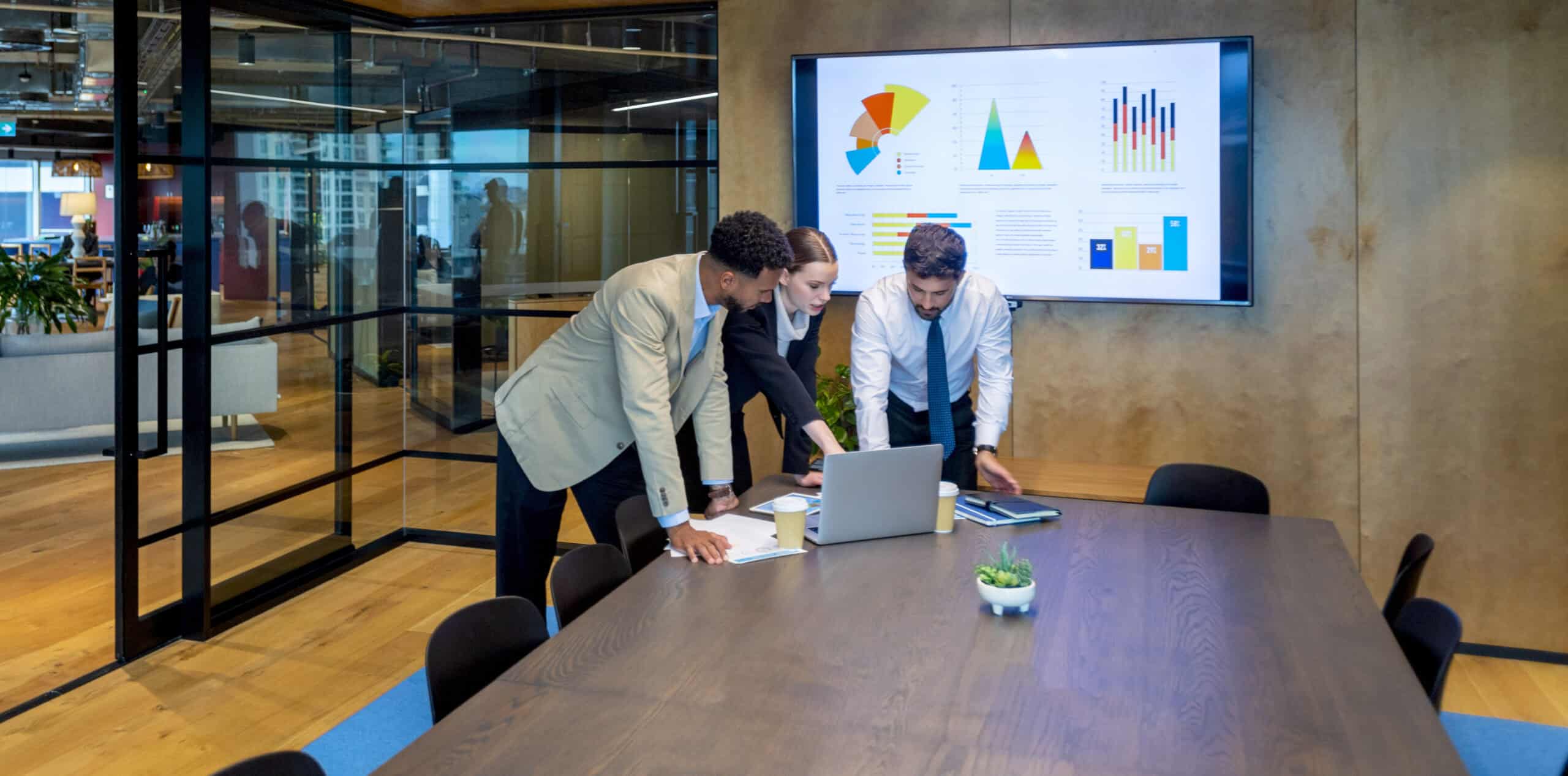 Collaboration among diverse professionals analyzing data on a laptop in a modern office setting, emphasizing the importance of teamwork in higher education and data-driven decision-making.