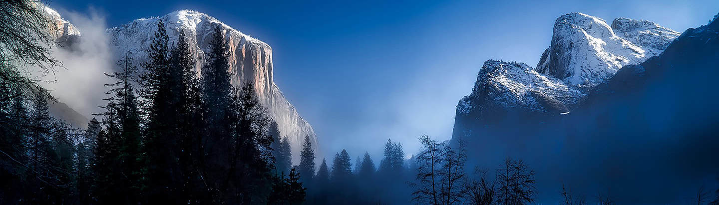 Majestic snow-capped mountains in Yosemite National Park with lush evergreen trees in the foreground, showcasing natural beauty and outdoor adventure opportunities.