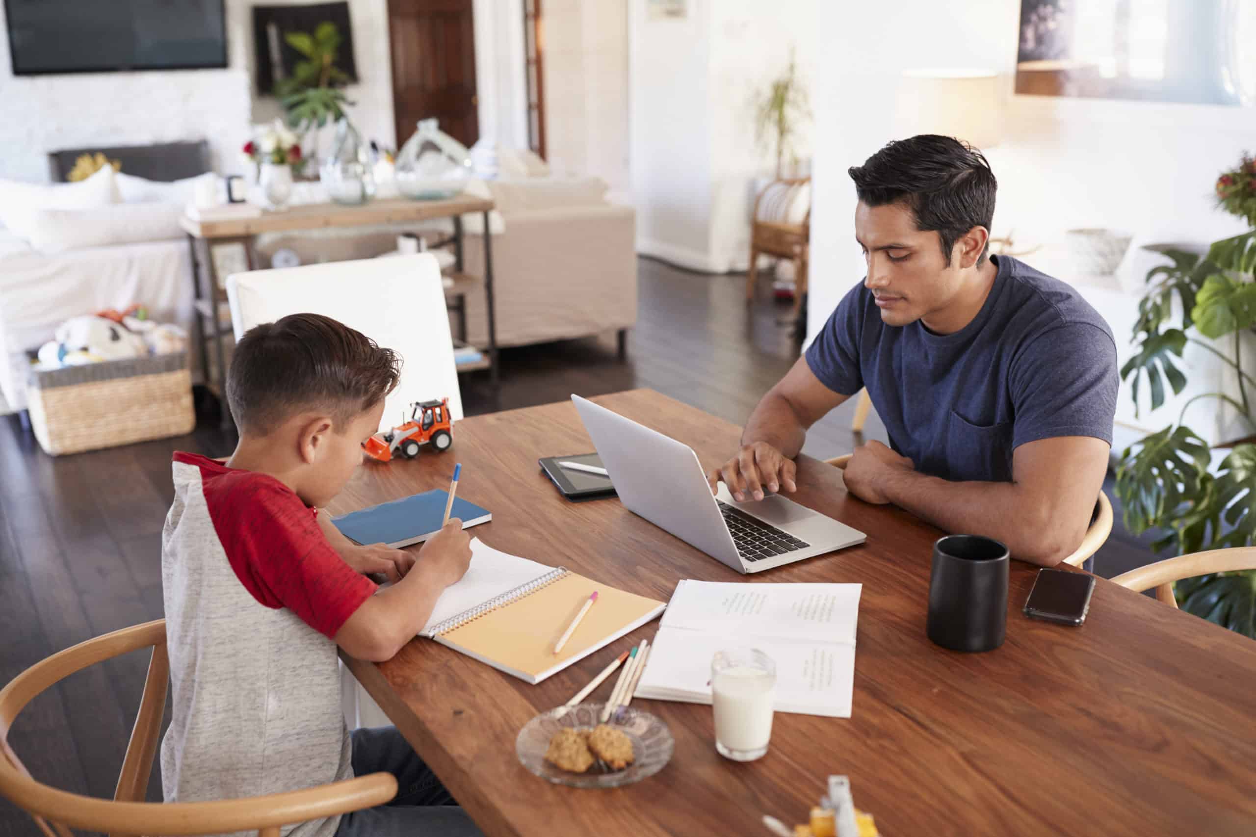 Working from home, father helping son with homework, online learning, remote education, digital study, parent and child studying, virtual learning environment, home study session, educational support, modern family home.