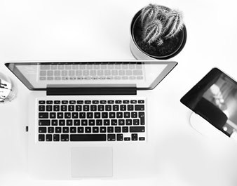 Laptop computer and smartphone on desk with coffee and glasses, representing higher education technology and student resources.