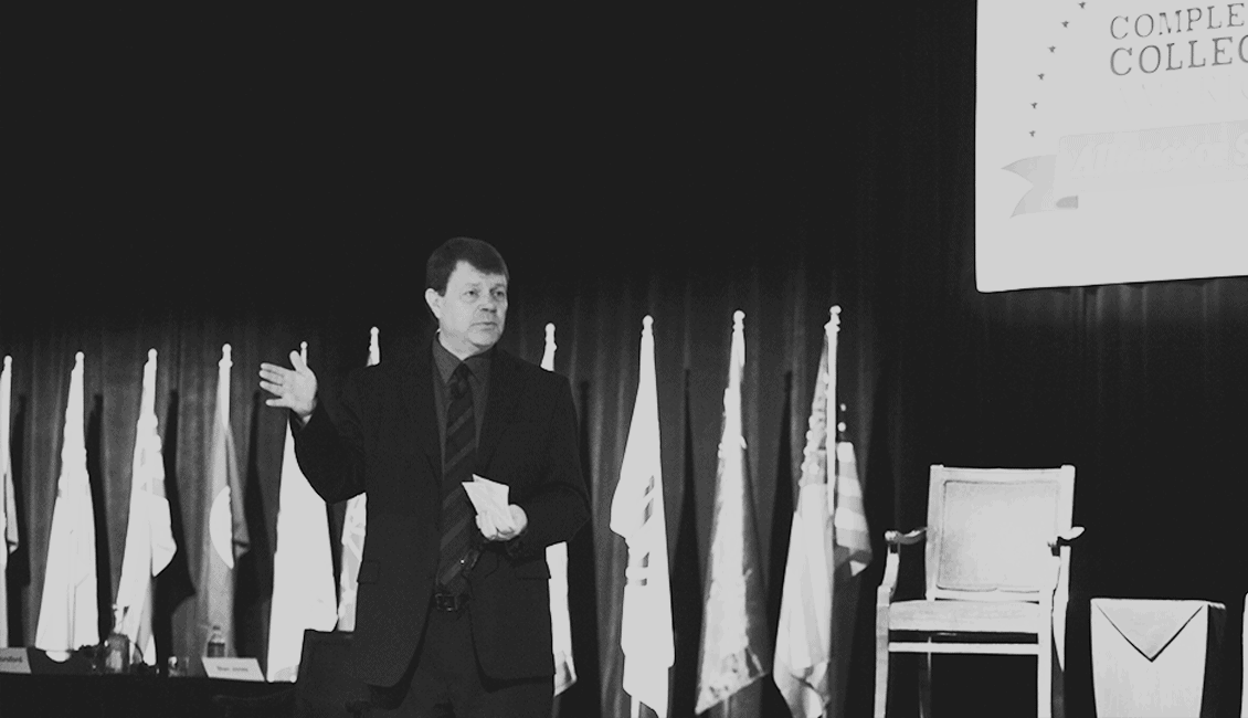 Study of a speaker presenting at Complete College America conference with multiple flags in the background, advocating for college success and higher education completion.