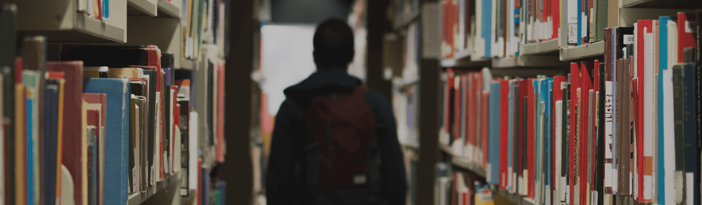 Student walking through library aisle with bookshelves on both sides, representing educational resources and college readiness for Complete College America.
