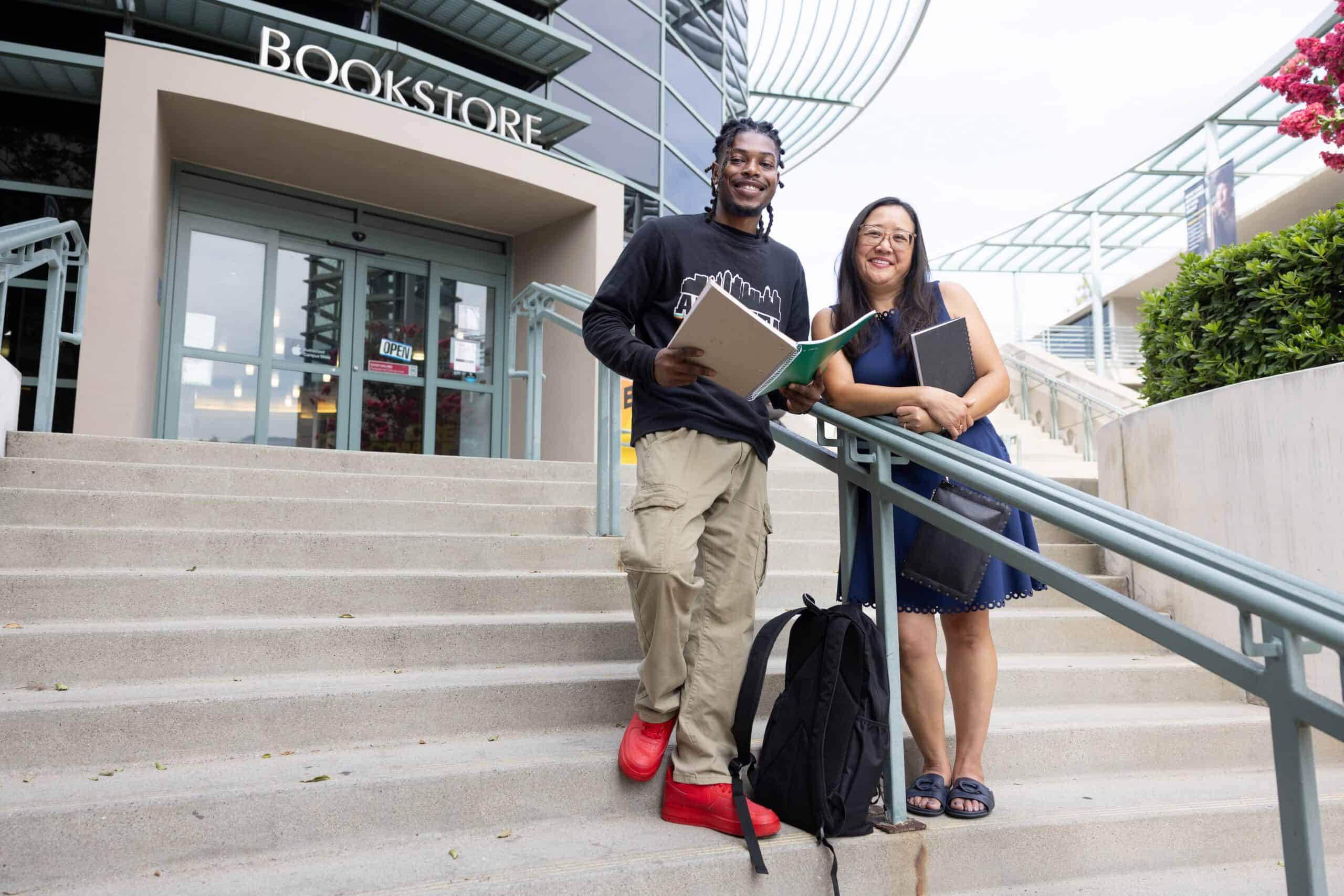 Bright smiling students standing on campus stairs outside the bookstore, holding notebooks and backpacks, representing higher education, college success, and student achievement.