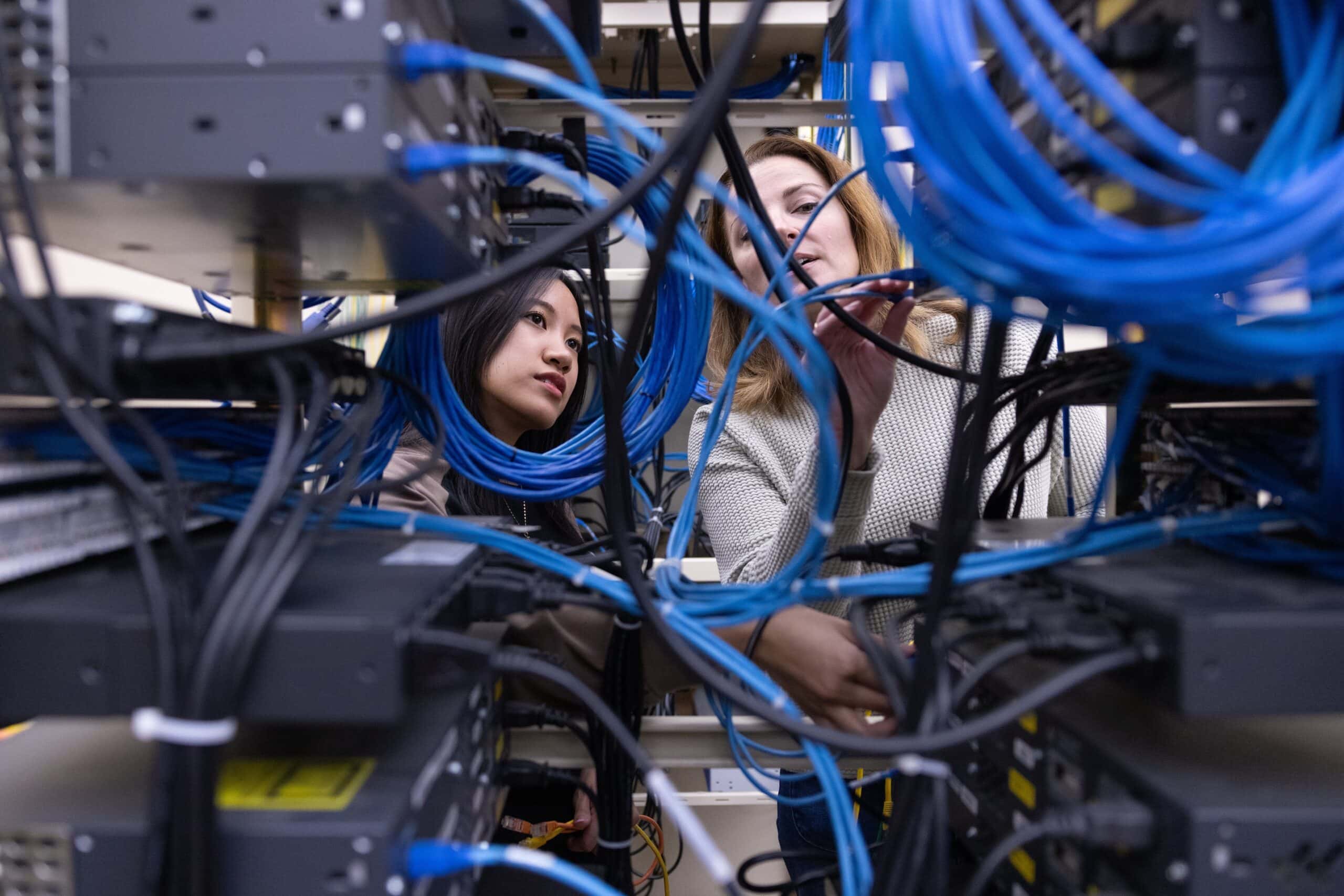 High-tech networking technicians working on server racks with blue Ethernet cables in a data center. Focuses on computer networking, internet infrastructure, and IT management.
