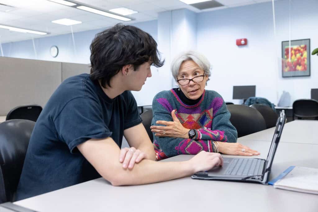 College student and adult advisor discussing academic success strategies at a computer in a meeting room.