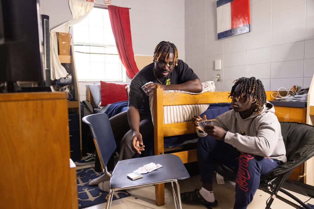 Fellow students playing cards and hanging out in a college dorm room, showcasing student life and campus community at Complete College America.