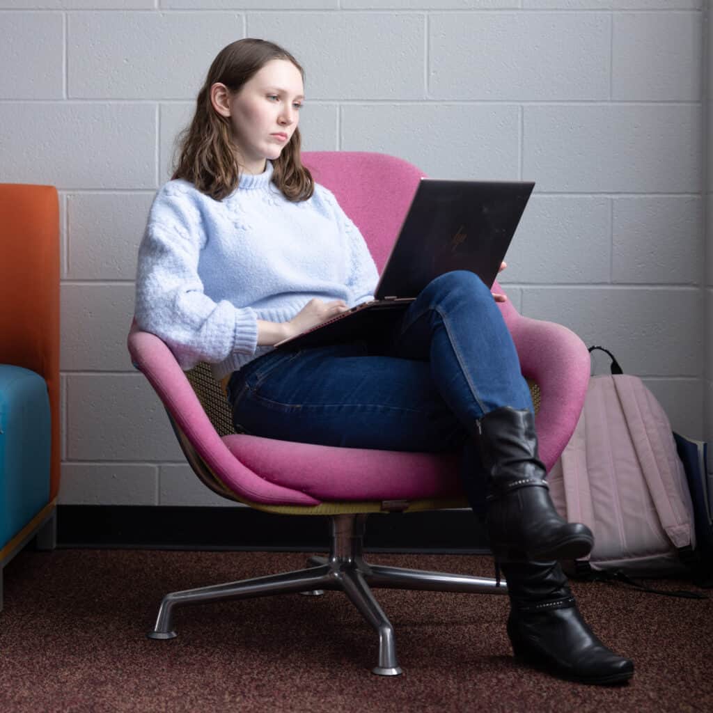 Focused college student studying on laptop in a college lounge.