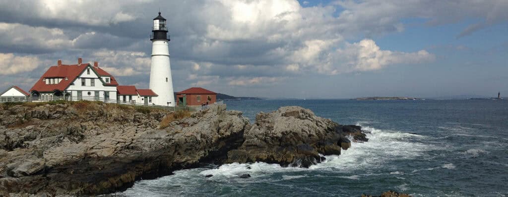 Lighthouse on rocky coast with ocean waves and cloudy sky, illustrating navigation and coastal safety.