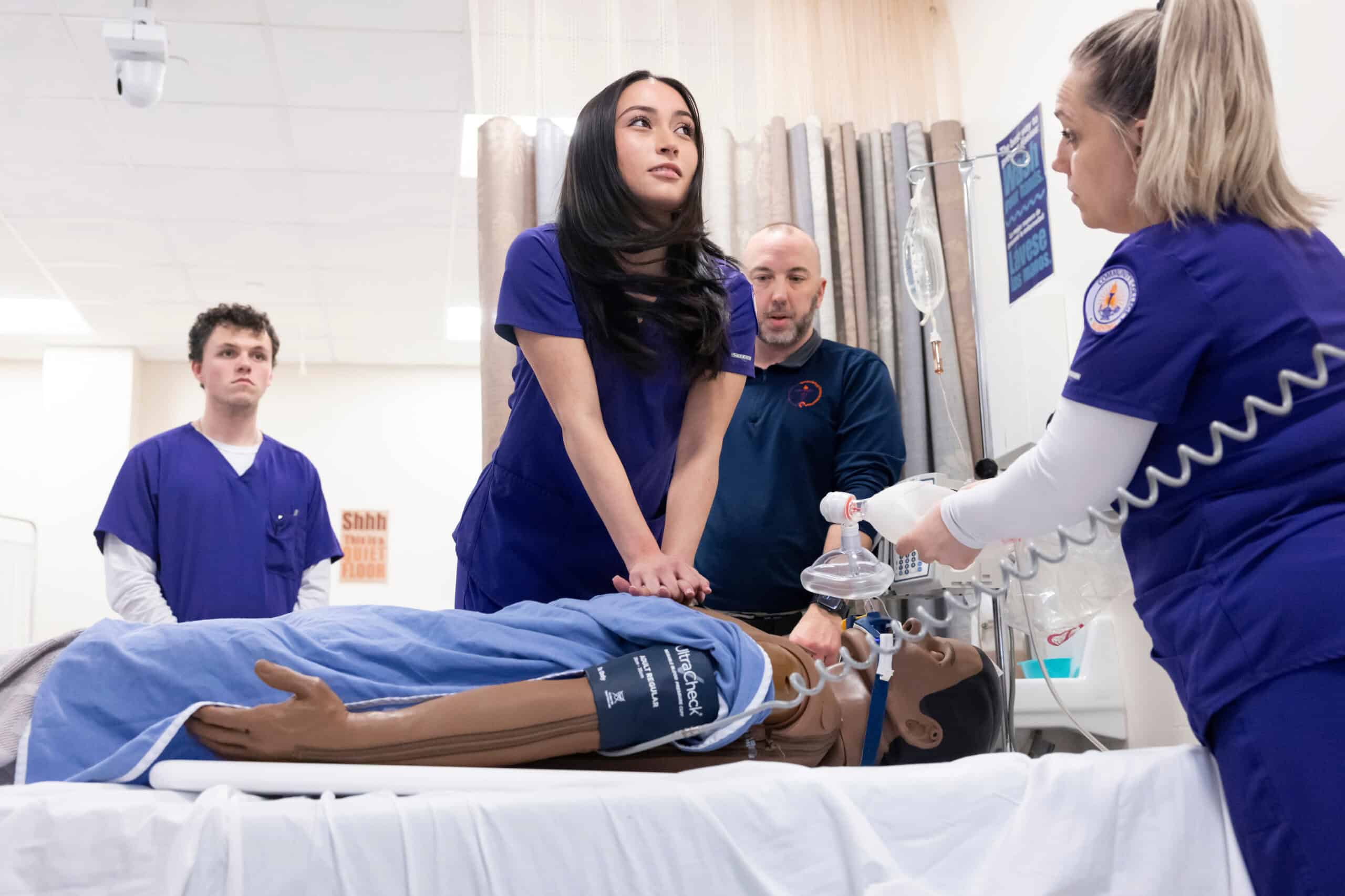 Highly skilled medical students practicing emergency response techniques on a mannequin in a clinical simulation training session.