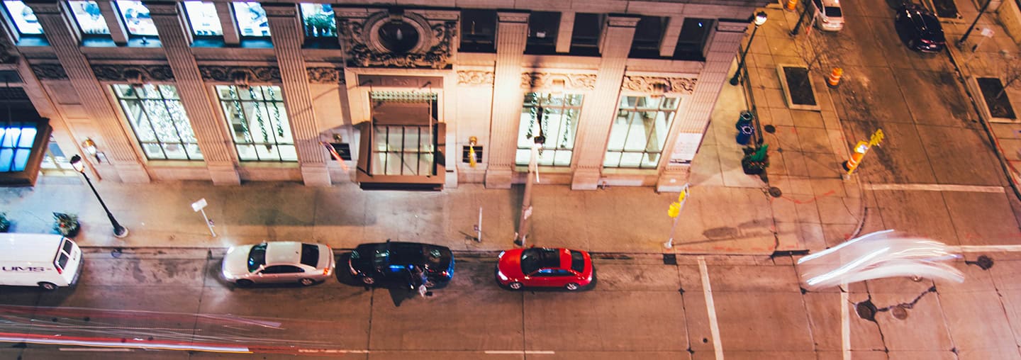 College street scene at night showing parked cars and illuminated historic building in downtown area.