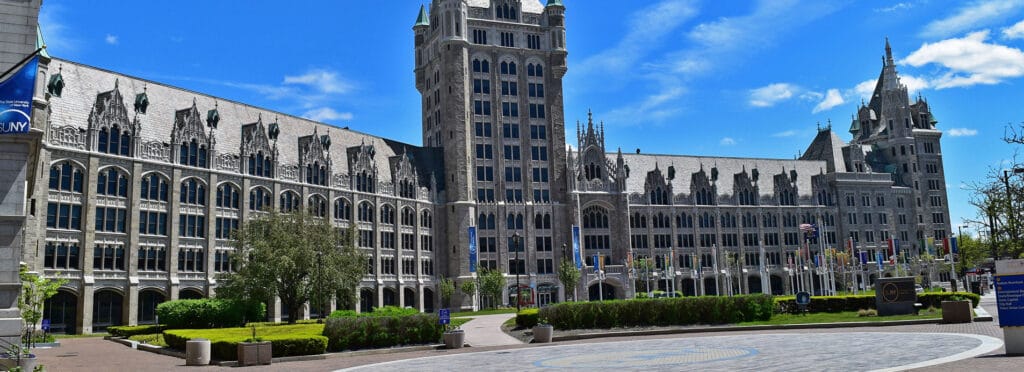Historic Gothic-style university building with towers and arched windows at SUNY campus in Albany, New York, under a bright blue sky.