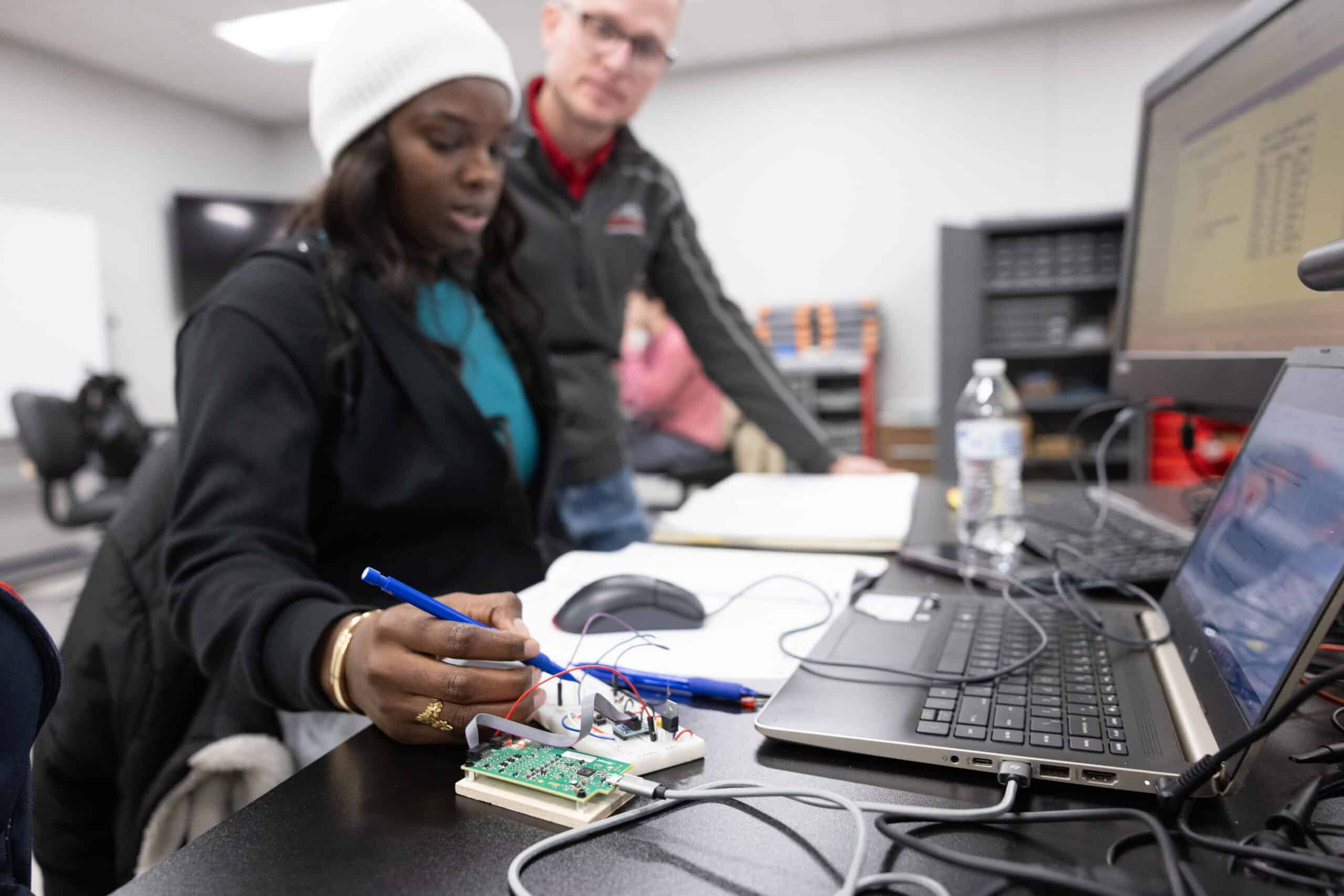 Innovative college students working on electronics project with laptop and circuit board, representing STEM education and technology training at Complete College America.