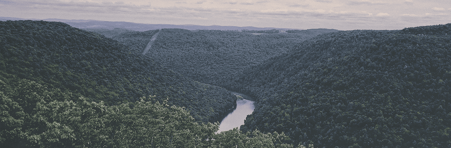 Hiking trail through lush green mountains and a winding river in a scenic natural landscape.