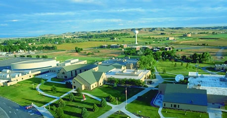 High school and college buildings in a rural educational campus with green fields and open skies, representing community higher education and college readiness.