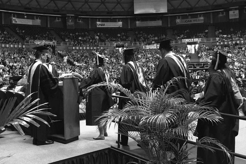 Graduates receiving diplomas at a college commencement ceremony in a large indoor arena focusing on higher education success.