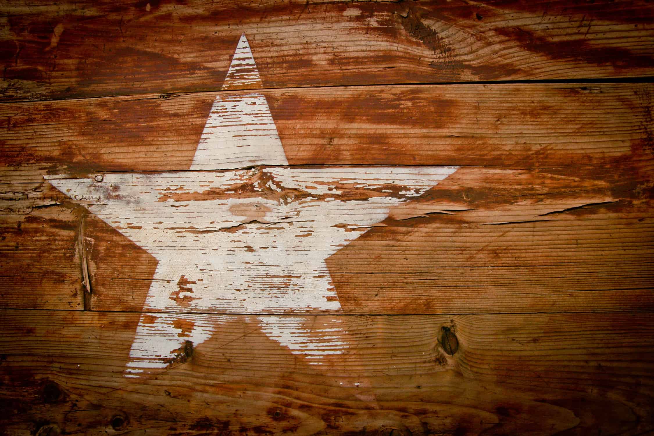 Weathered white star painted on rustic wood plank wall, symbolizing Texas pride, Americana, and leadership. Suitable for themes of education, community, and state pride.