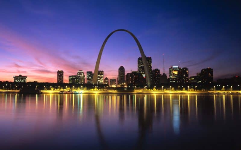 St. Louis skyline with Gateway Arch at sunset, reflecting on the Mississippi River, emphasizing urban development, education, and community growth.