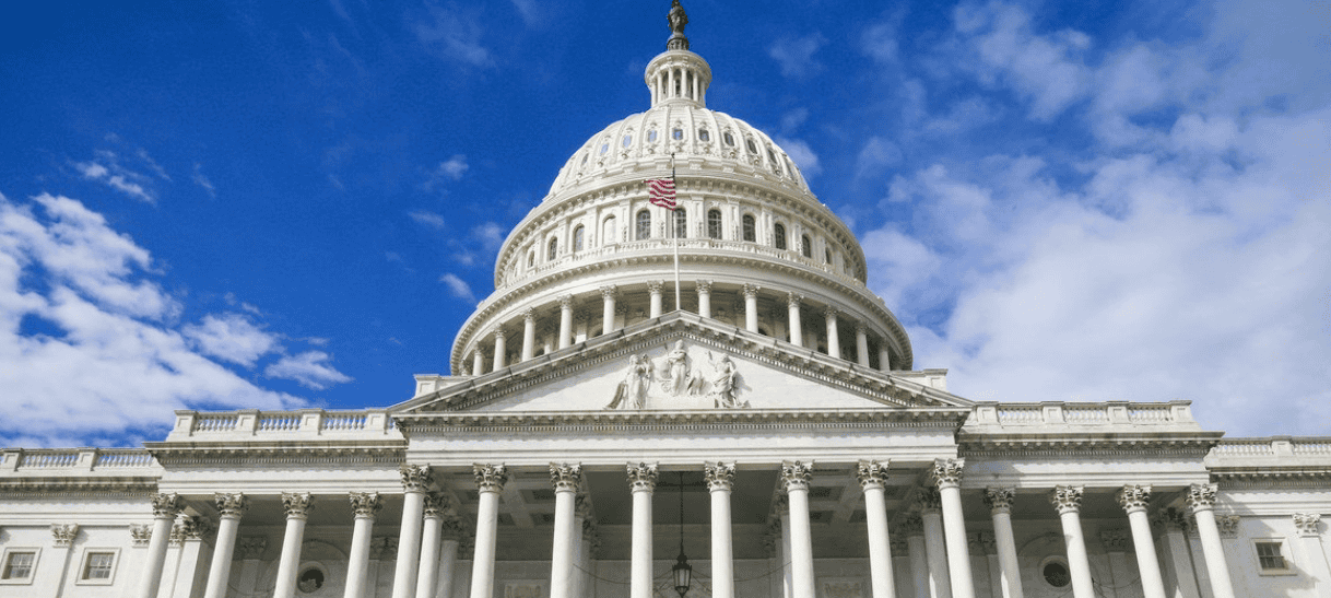 A white government capitol building with a prominent dome, set against a bright blue sky with scattered clouds, symbolizing education policy and access.