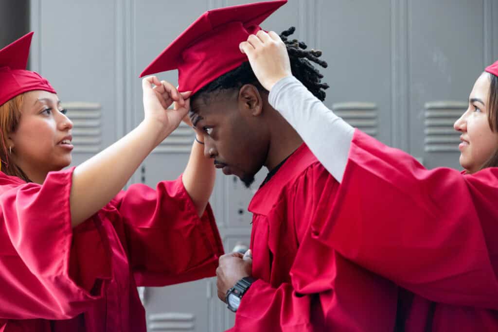 Graduating students in red caps and gowns preparing for commencement at a college or university.