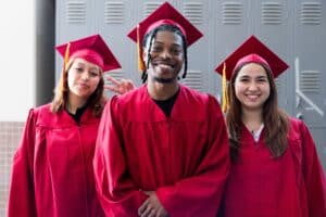 Diverse group of students in red graduation gowns celebrating success in higher education at a college campus.