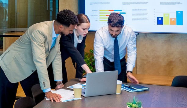 College team analyzing data on laptop in a meeting room for higher education strategies.