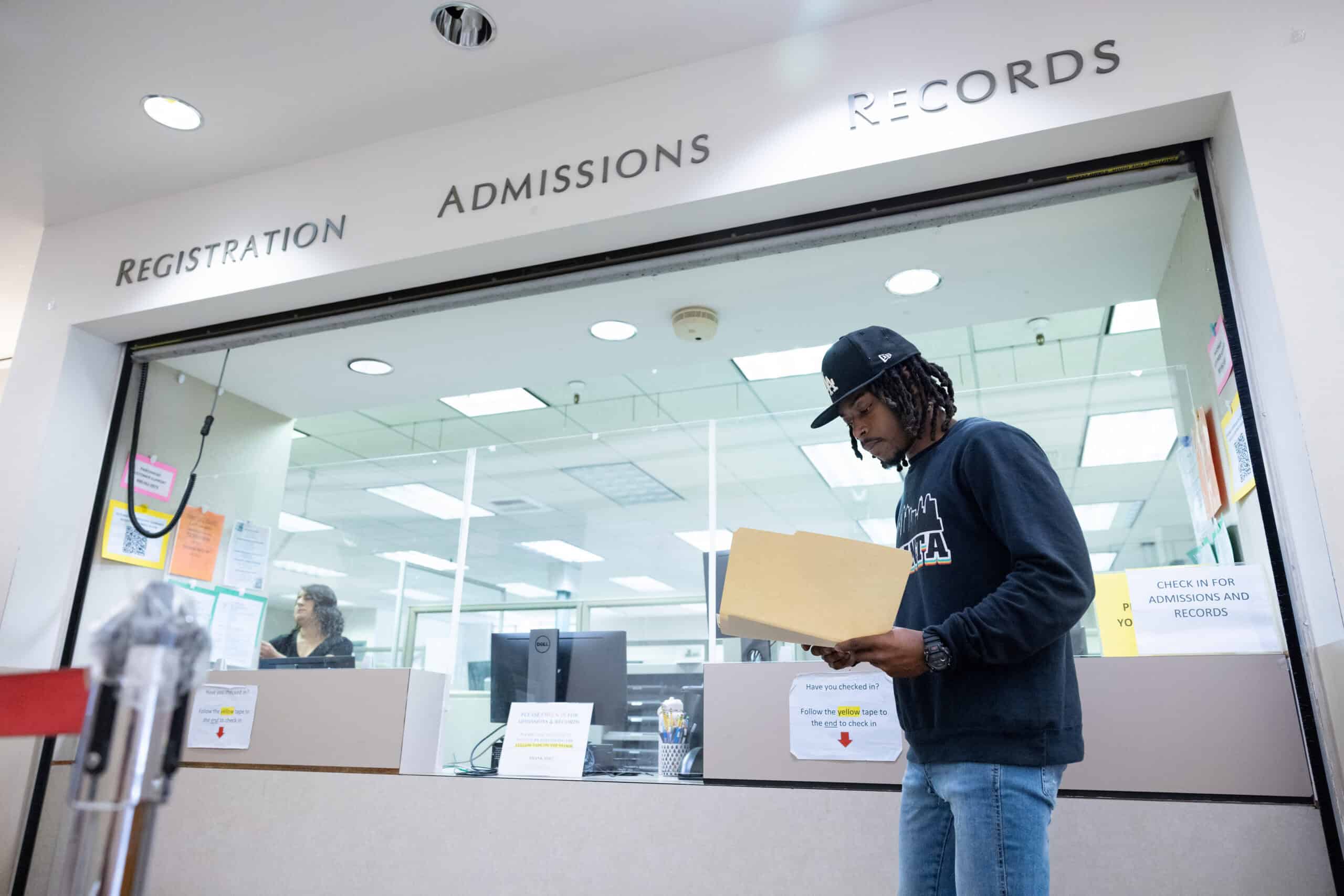 Black male student looking in a folder at the admissions, registration and records office on a college campus.