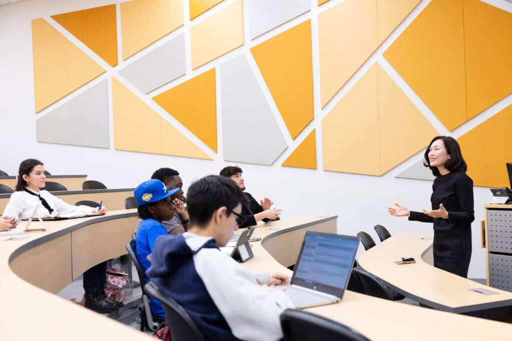 Multiethnic group of students listening to instructor in a large classroom on a college campus.