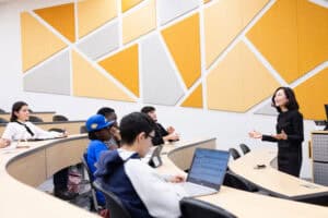Multiethnic group of students listening to instructor in a large classroom on a college campus.